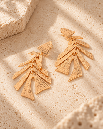 Pendientes Lola Casademunt dorados con diseño de hojas superpuestas y textura en relieve, colocados sobre una superficie de piedra beige