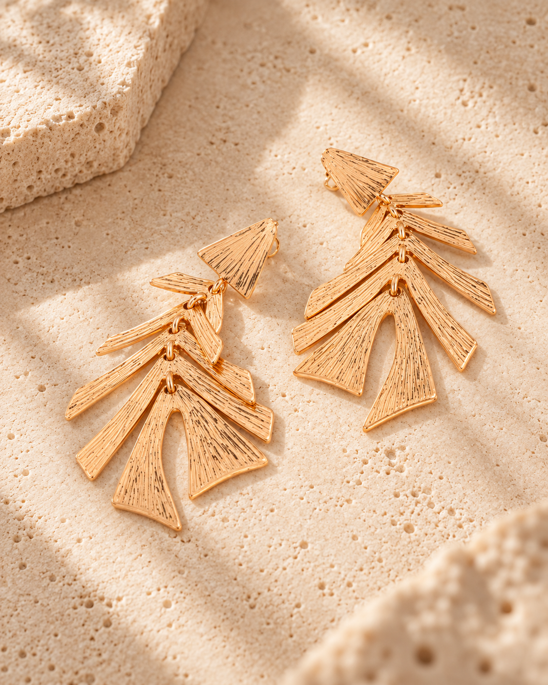 Pendientes Lola Casademunt hojas textura dorados - vista principal Pendientes Lola Casademunt dorados con diseño de hojas superpuestas y textura en relieve, colocados sobre una superficie de piedra beige