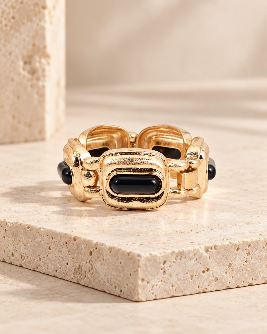 Pulsera Lola Casademunt medallones acrílicos negro y dorado - detalle Pulsera Lola Casademunt elástica con medallones acrílicos dorados y detalles negros, sobre pedestal de piedra beige