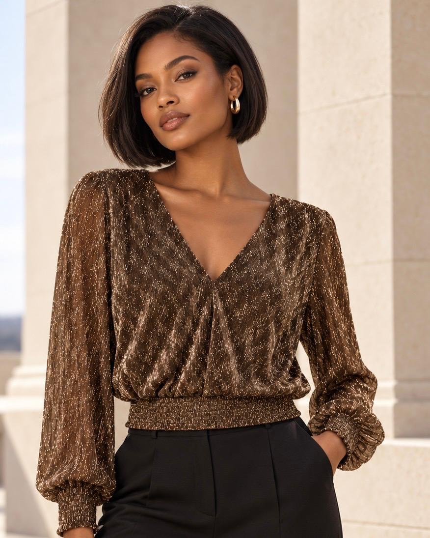 Top Morgan Tset bronce brillante con escote en V – vista frontal Modelo con top Morgan Tset bronce brillante de escote en V, mangas largas abullonadas y cintura fruncida, combinado con pantalón negro.